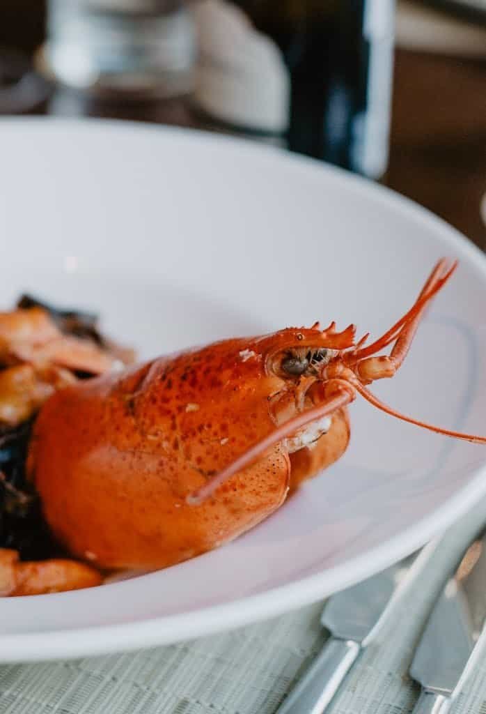 From above of appetizing lobster served on plate placed on napkin near cutlery on wooden table