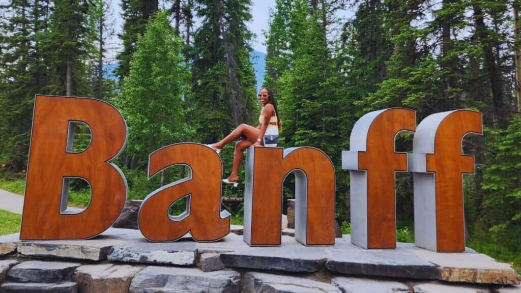 The author seated on the N of the Banff sign, perfect for a Banff National Park itinerary