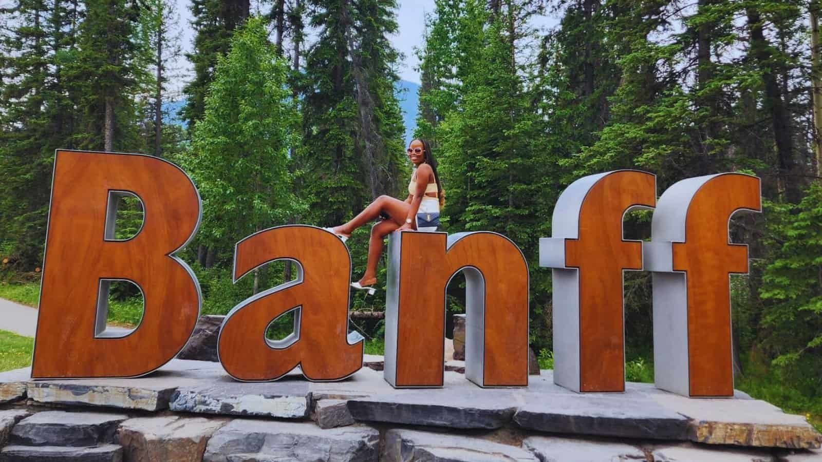 The author seated on the N of the Banff sign, perfect for a Banff National Park itinerary